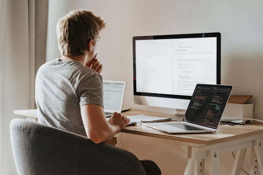A Mac user weighing options at a desk with an iMac and two MacBooks open in front of them